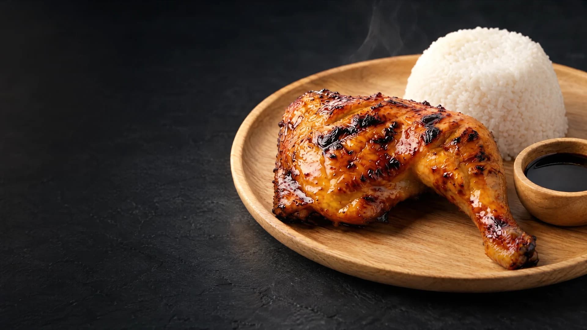 Chicken inasal with a dome of rice and soy dipping sauce on a wooden plate