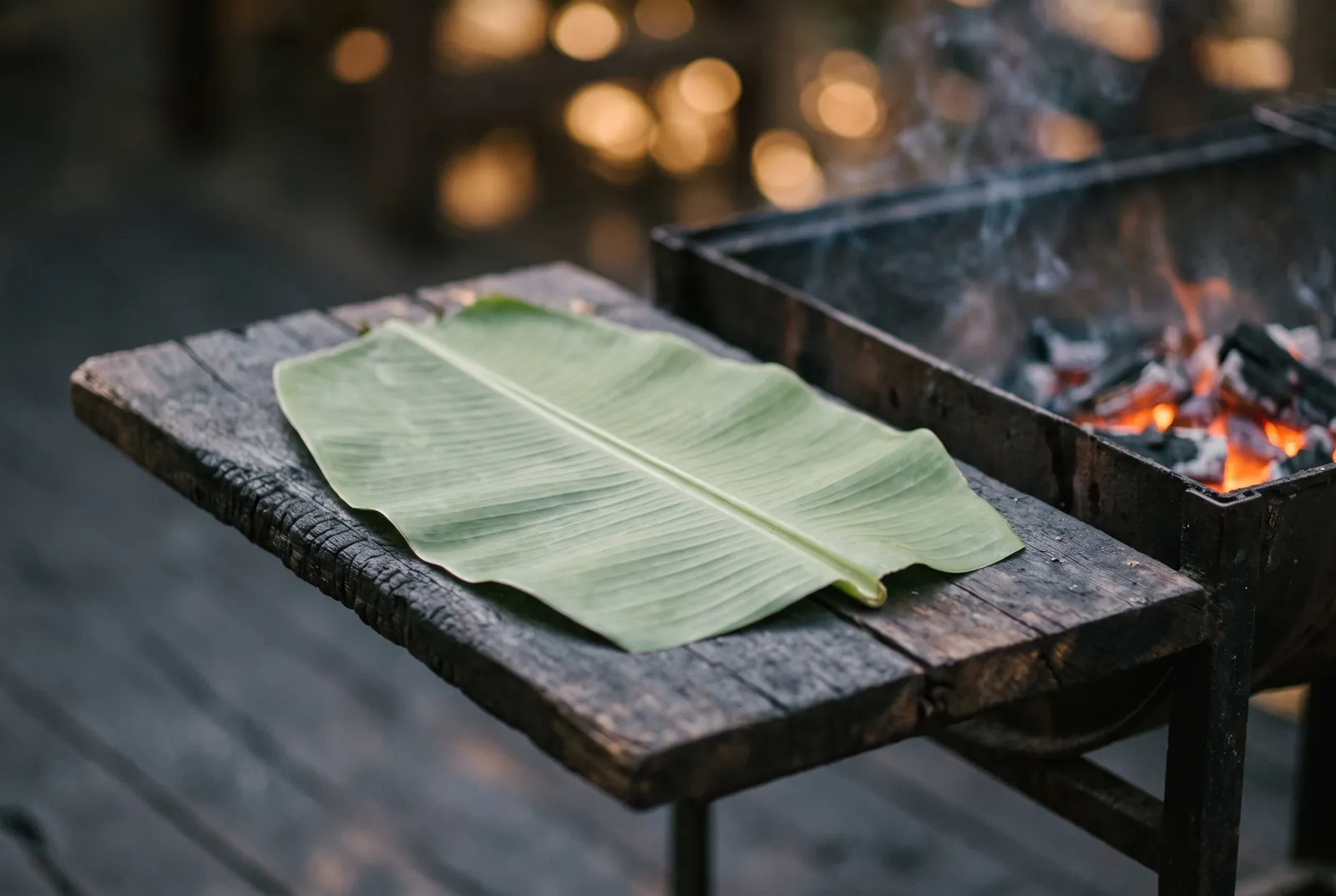 Banana leaf on a weathered board beside a charcoal grill